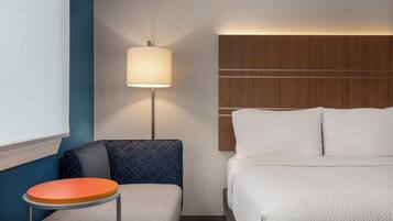 A hotel room with a bed, a nightstand with a lamp, a small table, and a blue wall.