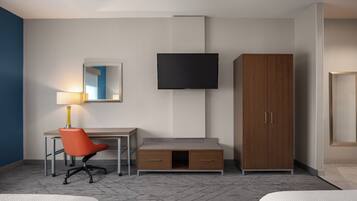 A hotel room with a desk, chair, wardrobe, TV, and two beds.
