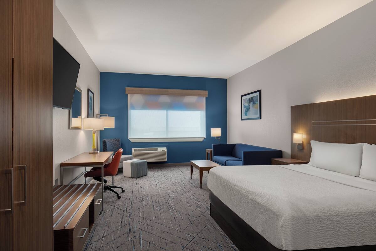 A hotel room with a bed, desk, chair, and a sofa.