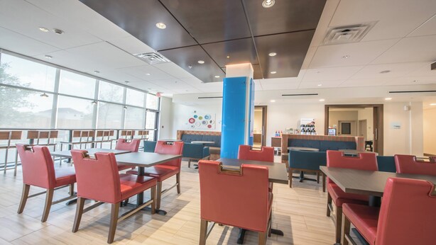 A modern dining area with red chairs and tables, large windows, and a blue pillar.