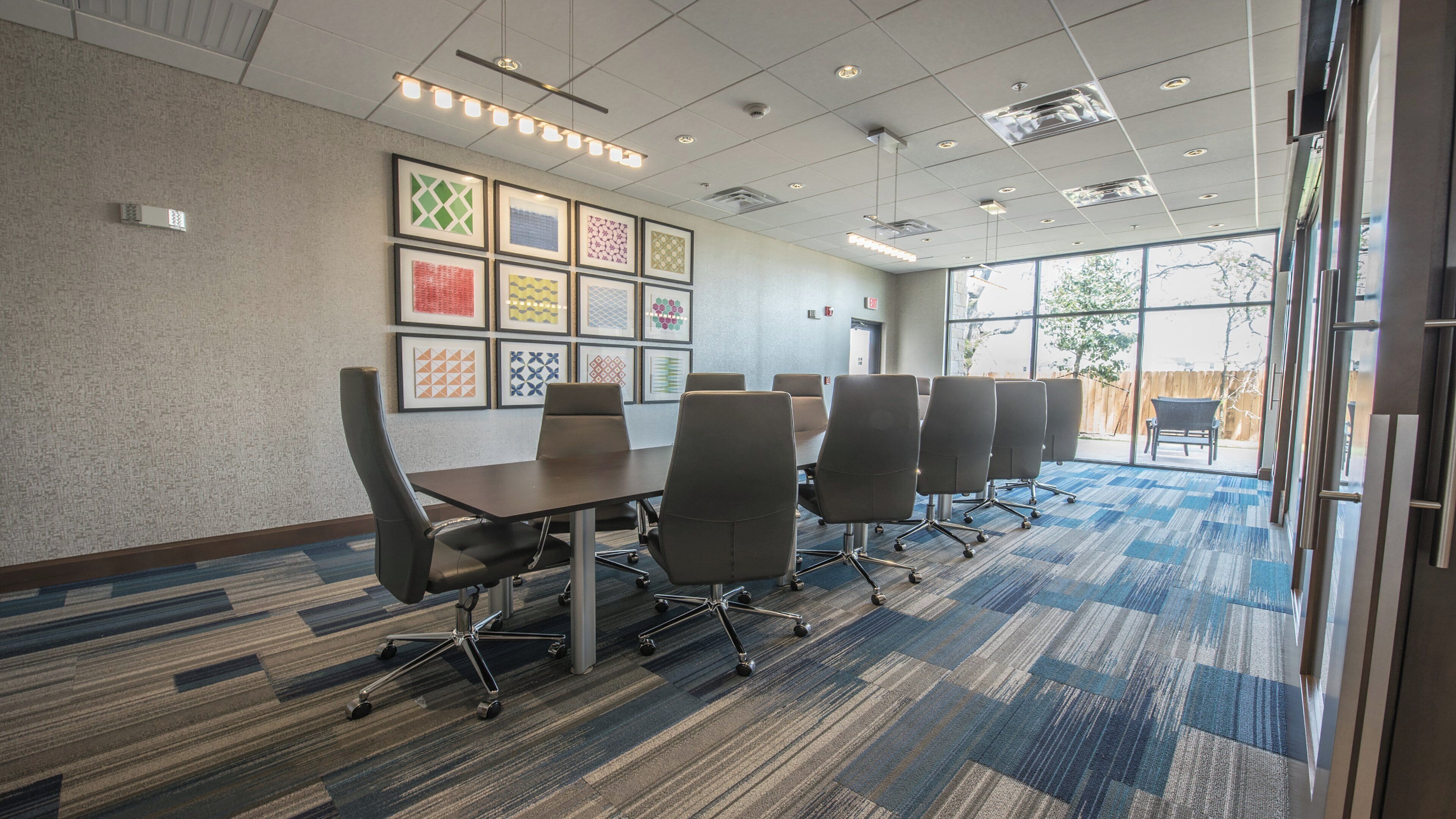 A conference room with a long table, six chairs, and framed artwork on the wall.