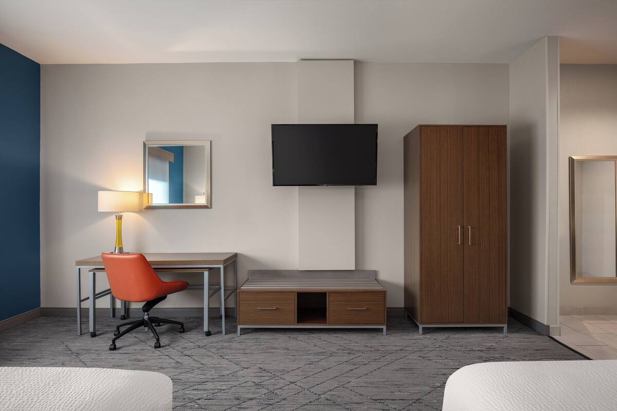 A hotel room with a desk, chair, wardrobe, TV, and two beds.