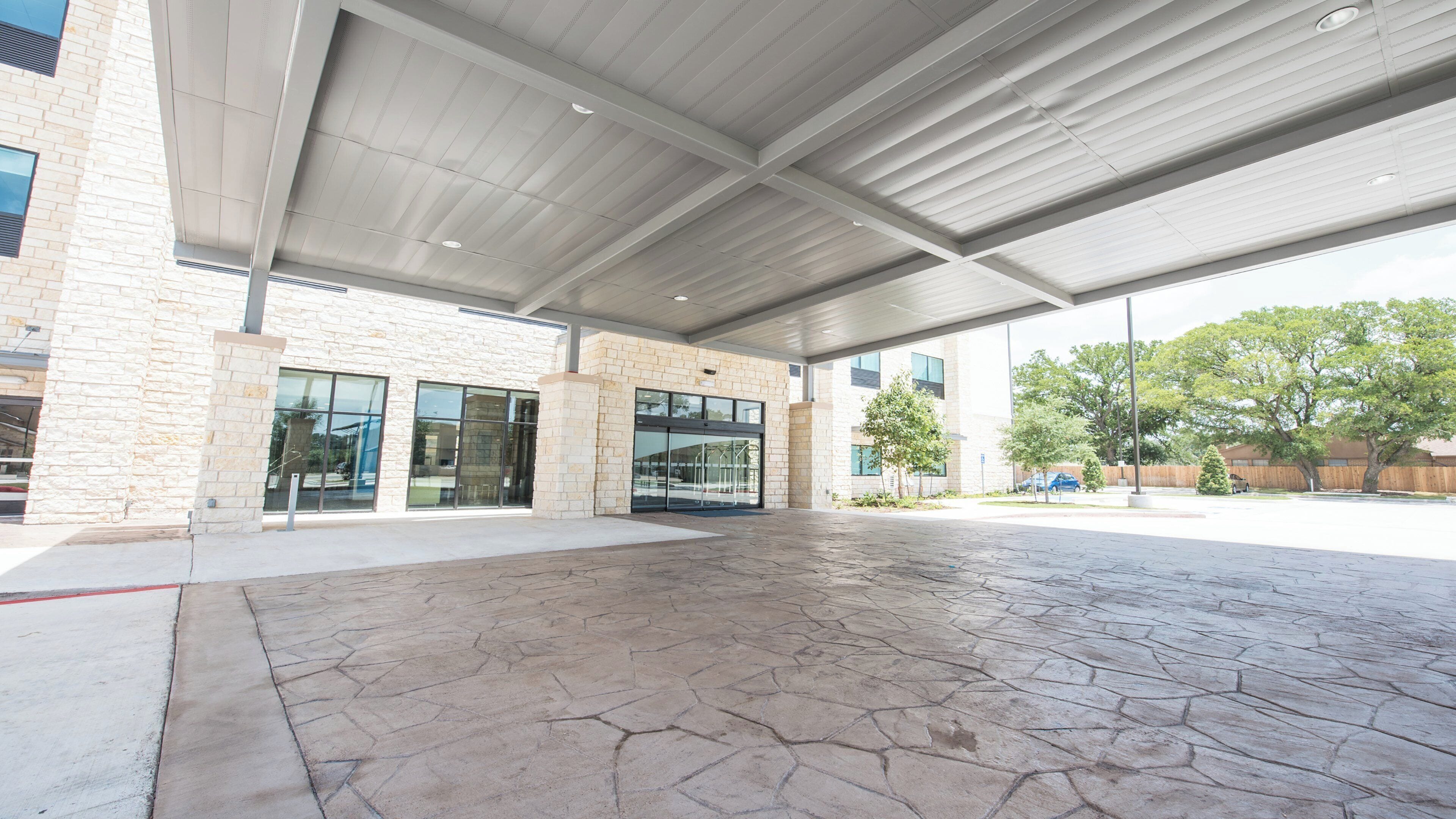 An outdoor covered area with a stone floor, large windows, and a building with a stone facade.
