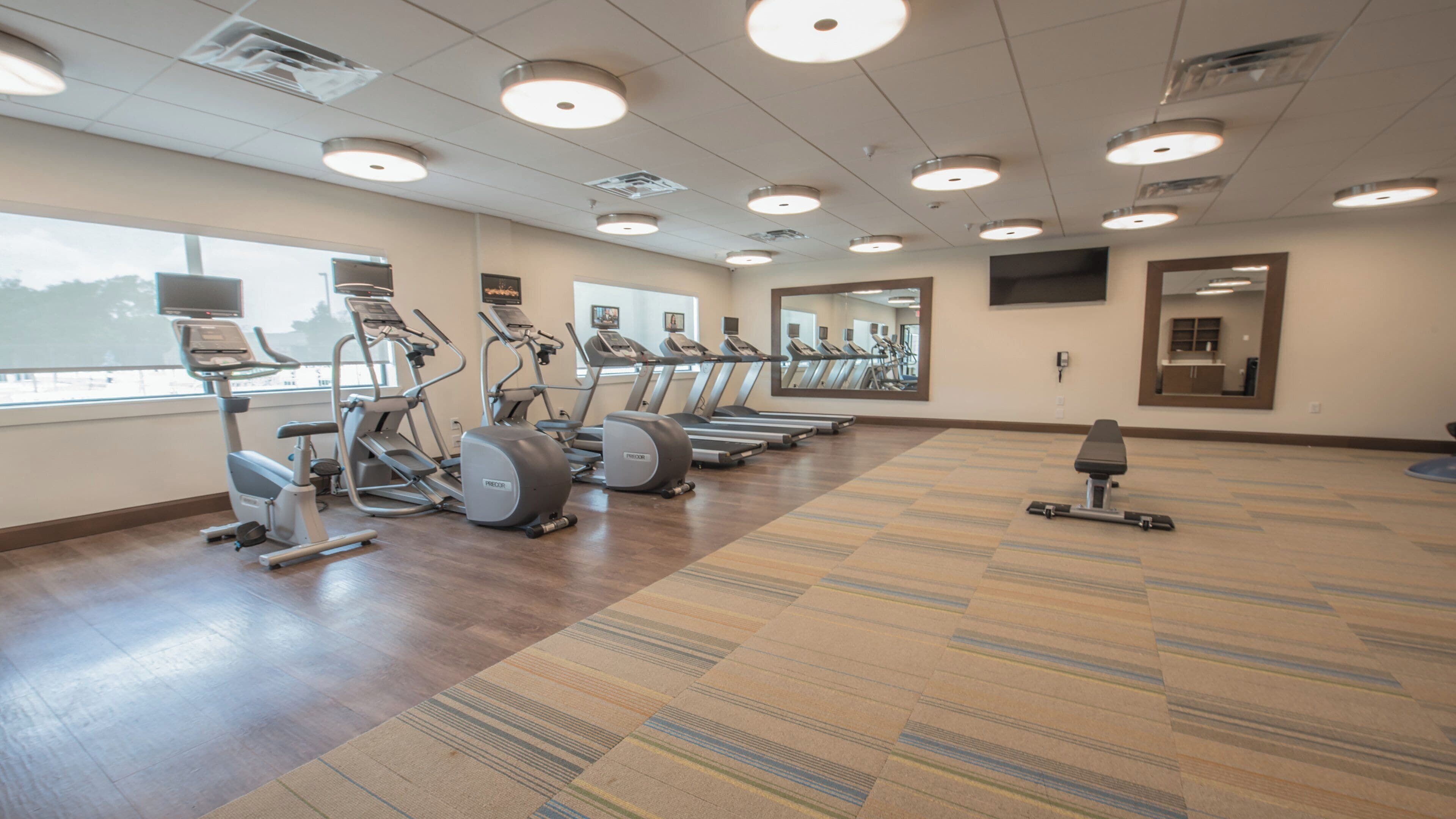 A gym with treadmills, elliptical machines, and a bench.