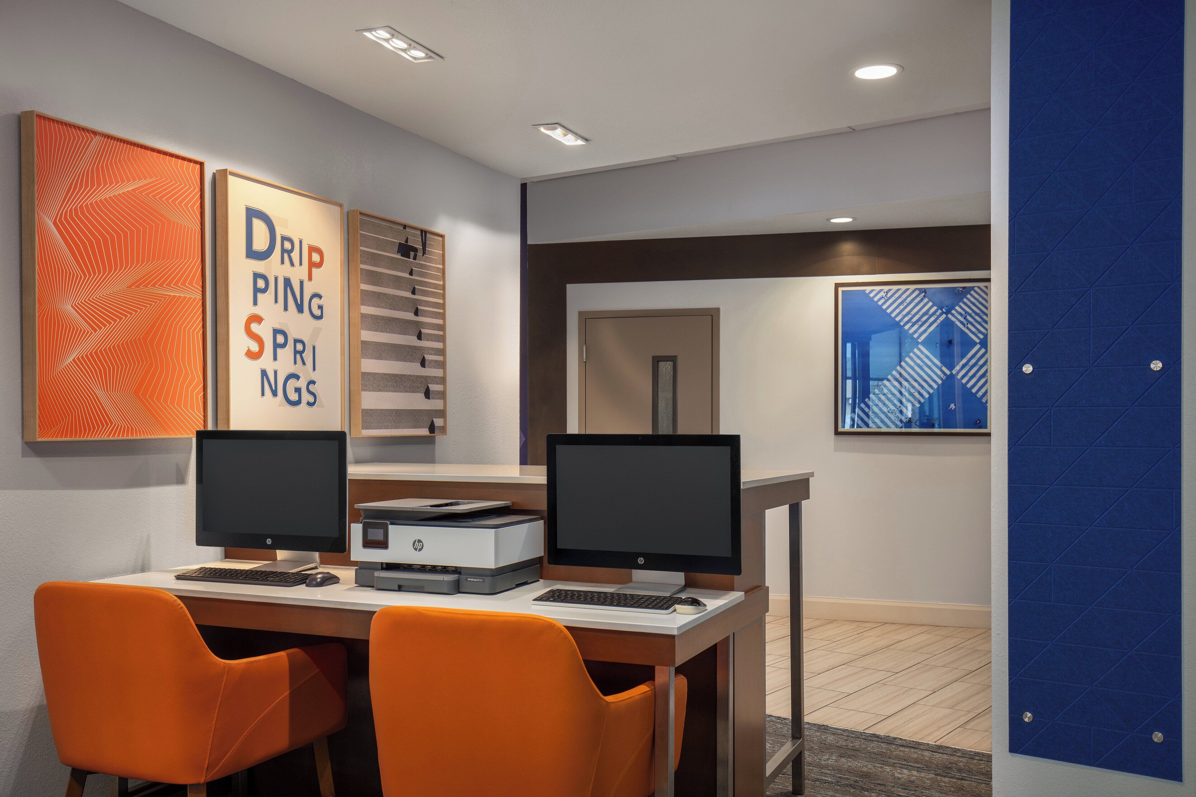 A modern office space with two desks, each with a computer and printer, and orange chairs.