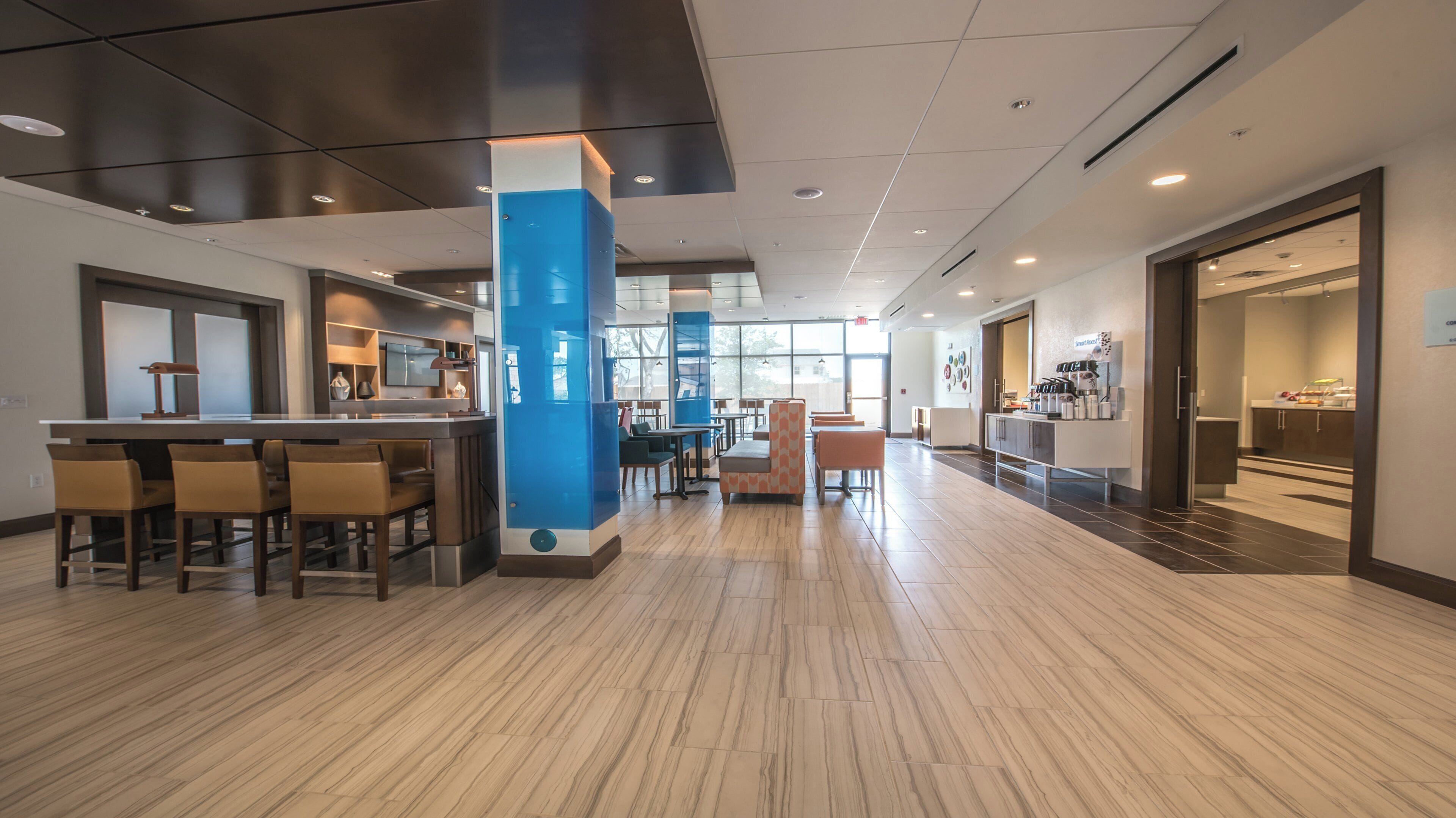 A modern hotel lobby with a bar area, seating, and a view of the outdoors.