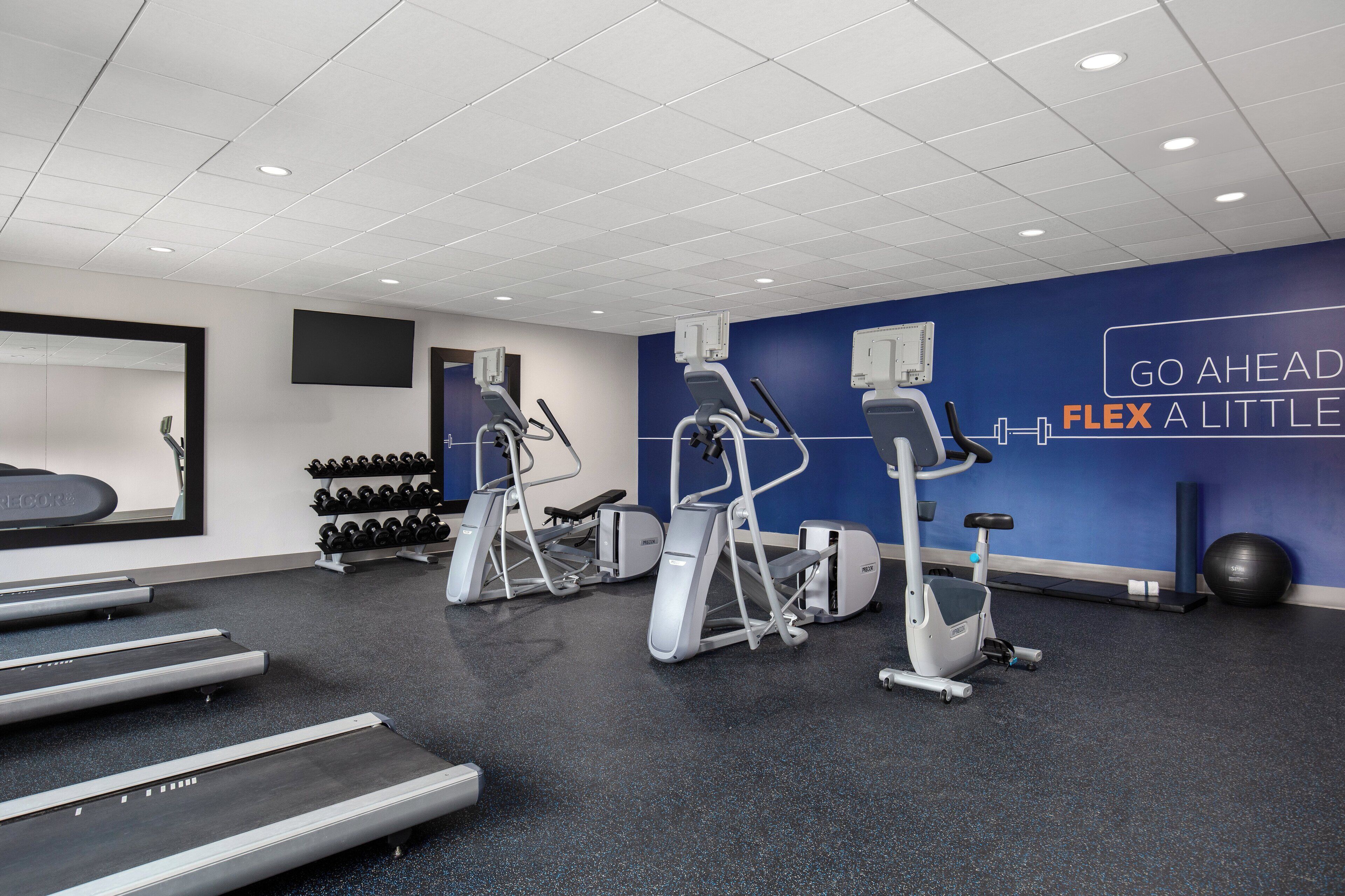 Et moderne fitnesscenter med løbebånd, crosstrainere og en motiverende væg.