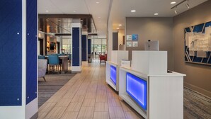 A modern hotel lobby with a reception desk, seating area, and a view of the dining space.