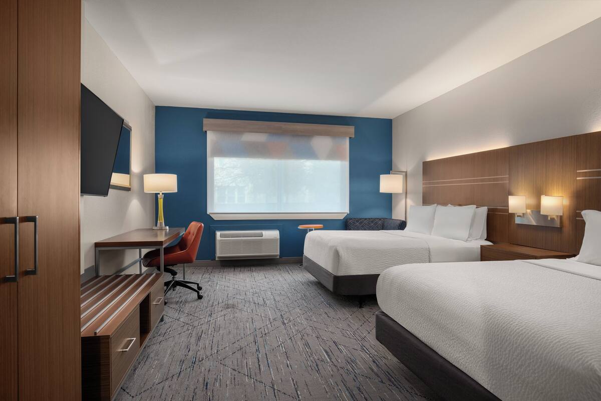 A hotel room with a desk, two beds, a TV, and a large window with a view.