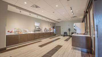 A modern hotel lobby with a reception desk, a digital screen, and a self-service beverage station.