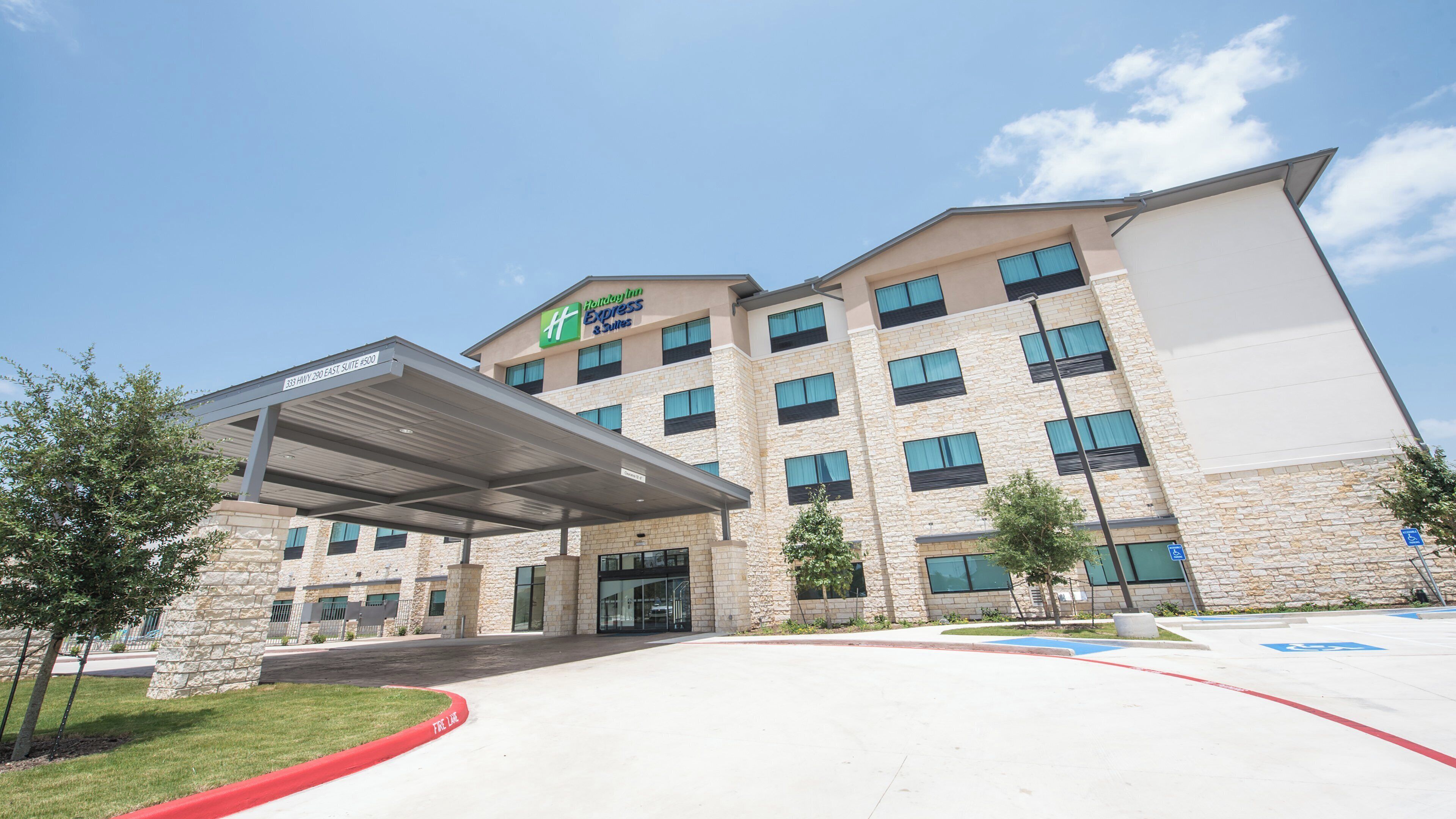 Un hotel Holiday Inn Express & Suites con entrada cubierta, fachada de piedra y múltiples ventanales.