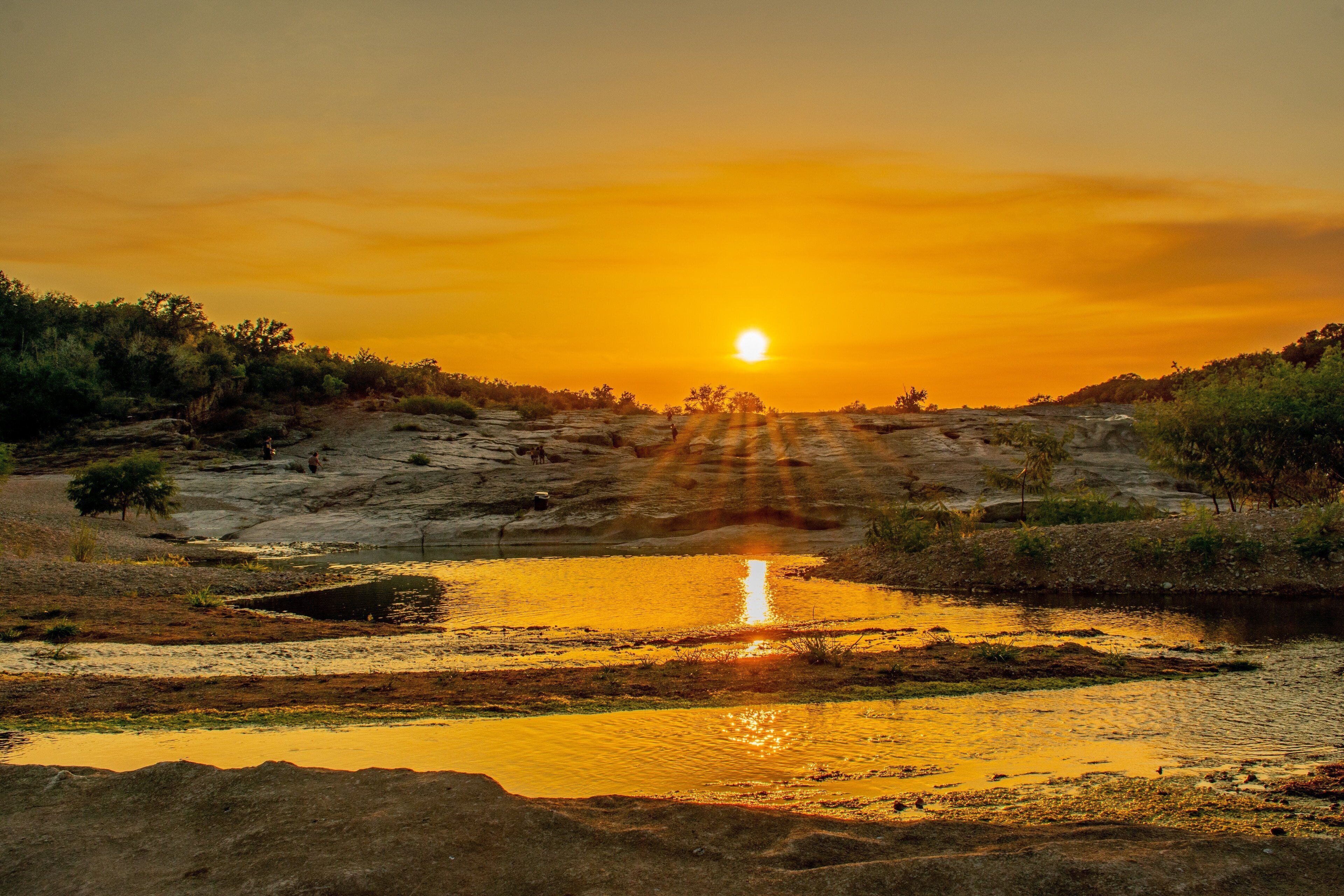 A sunset over a rocky landscape with a body of water reflecting the sky.