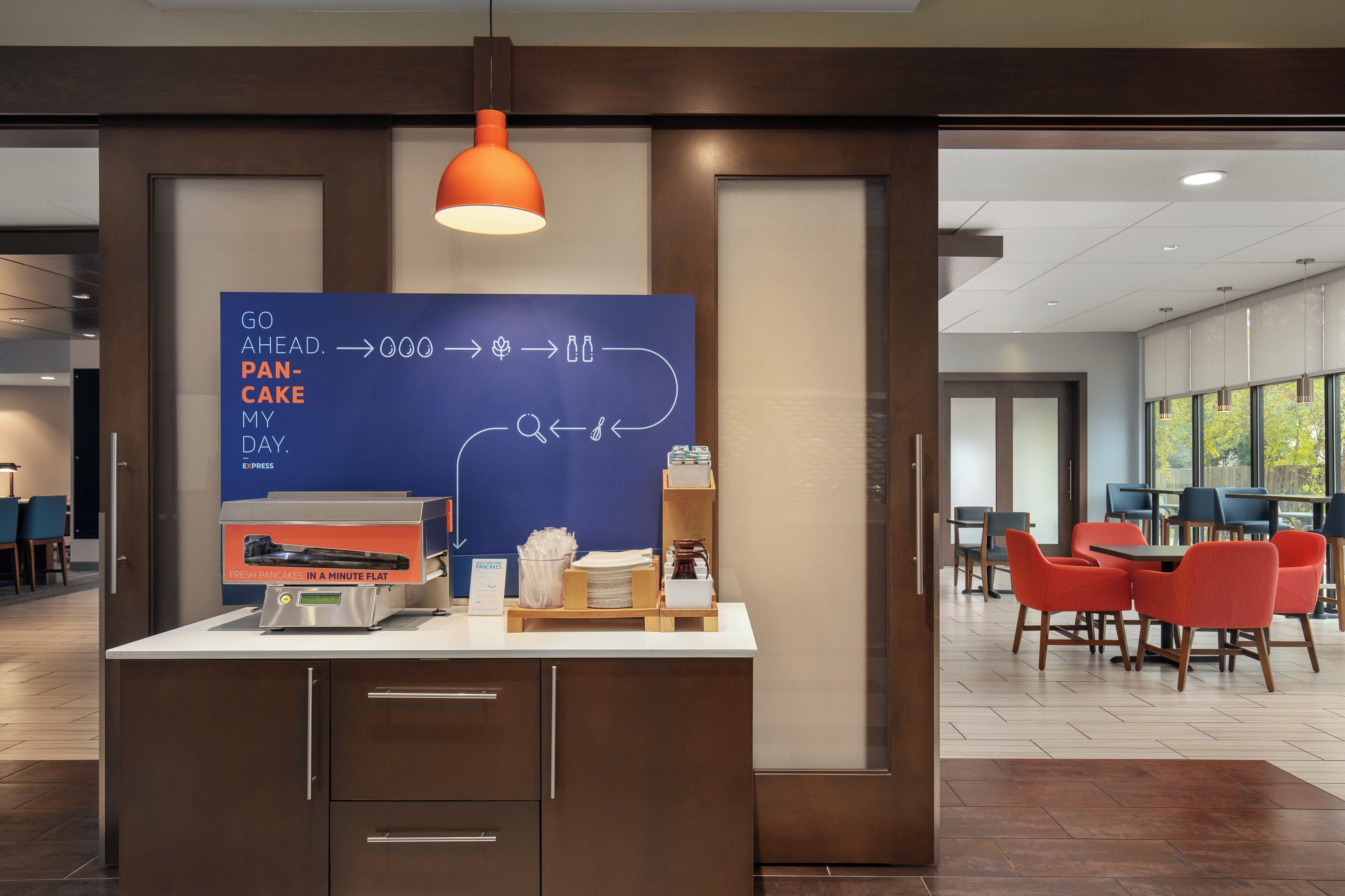 Un coin petit-déjeuner avec un panneau bleu, une machine à café et des chaises orange dans un espace repas moderne.
