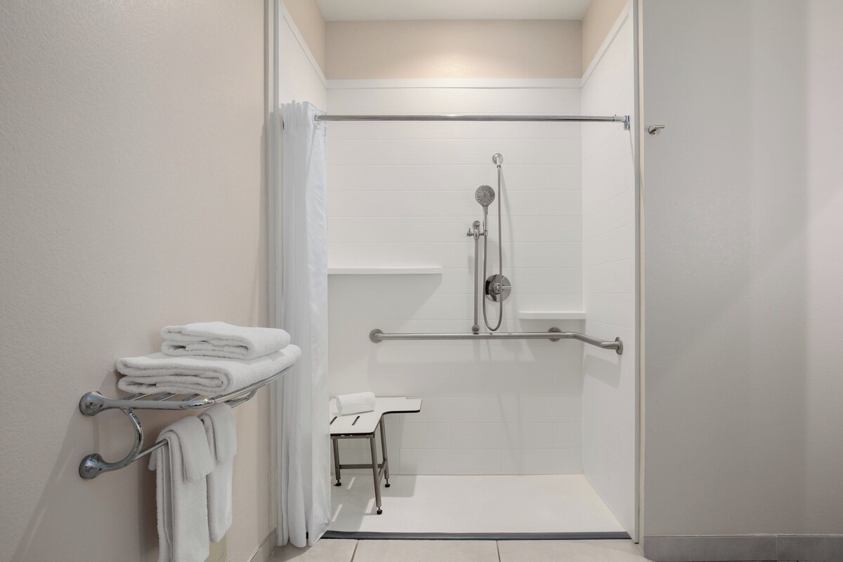 A modern bathroom with a walk-in shower, grab bars, and a towel rack.