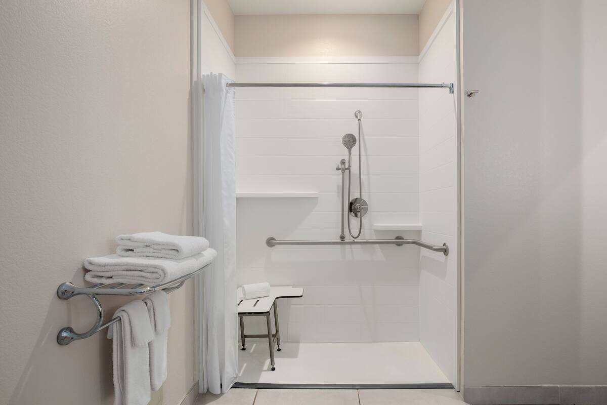 A modern bathroom with a walk-in shower, grab bars, and a towel rack.