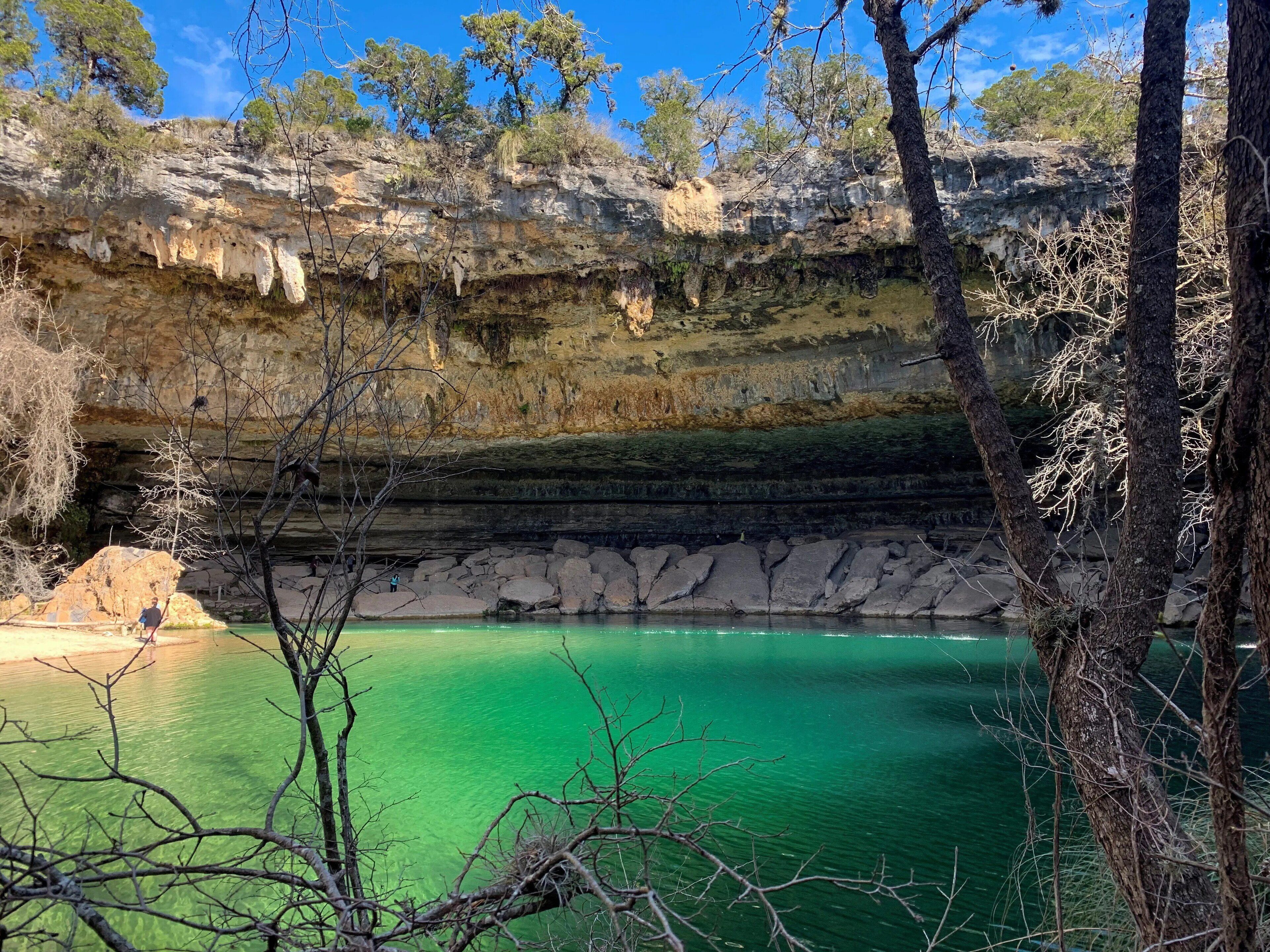 Un paysage naturel caractérisé par un lac aux eaux d’un vert limpide, des falaises rocheuses et une végétation arbustive clairsemée.