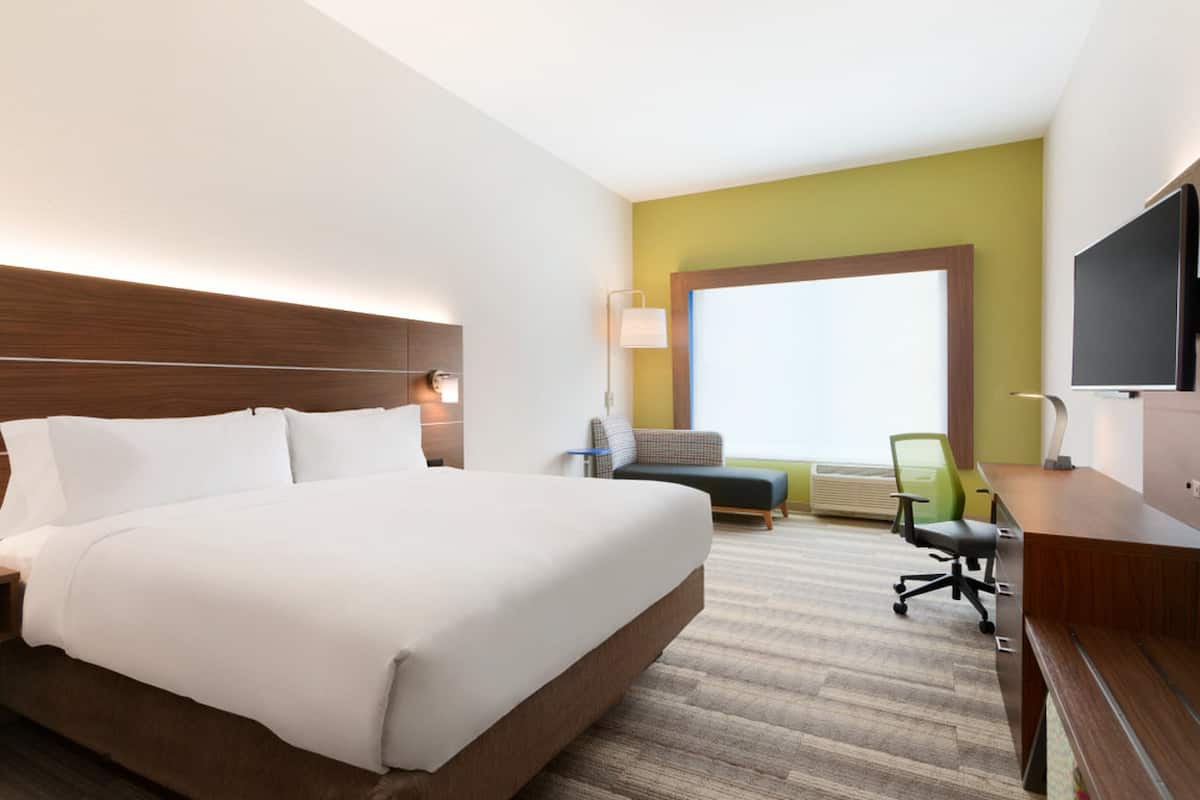 A hotel room with a large bed, a desk, a chair, a TV, and a window.
