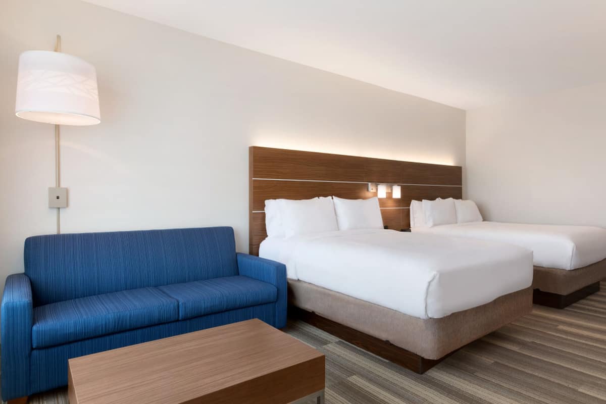 A hotel room with a blue sofa, a wooden coffee table, and a bed with two white pillows.