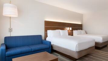 Una habitación de hotel con un sofá azul, una mesa de centro de madera y una cama con dos almohadas blancas.
