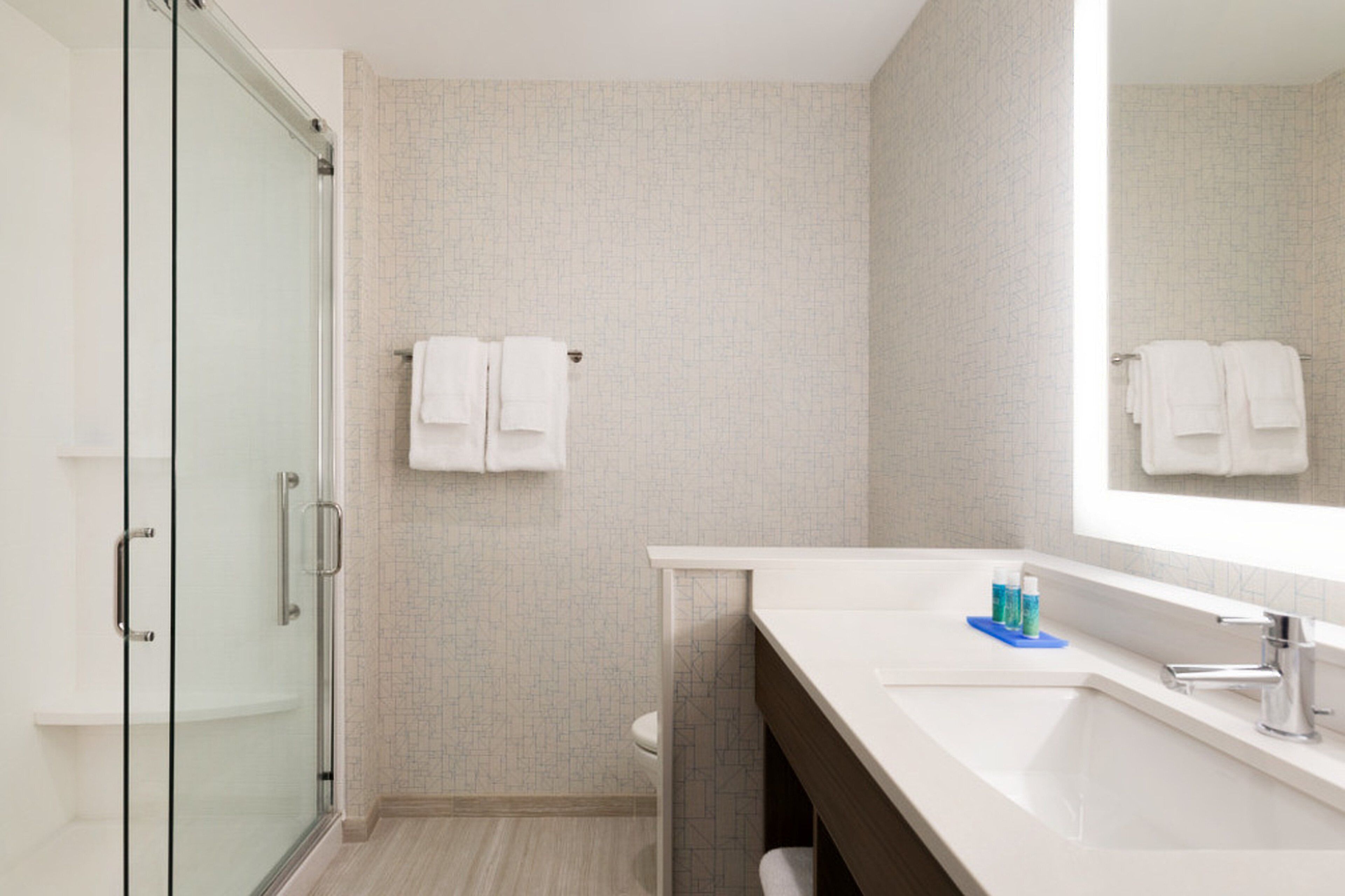 A modern bathroom with a glass shower enclosure, a white sink with a mirror, and a towel rack with two towels.
