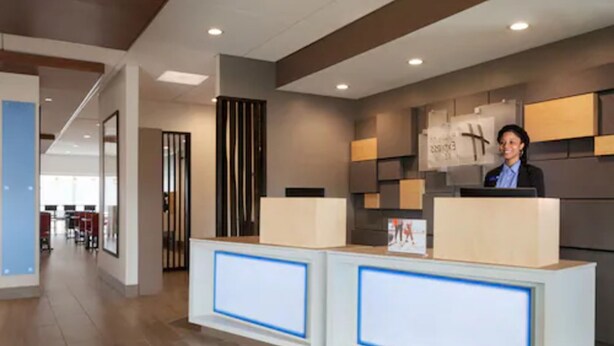 A reception area with a modern design, featuring a reception desk, a large clock, and a framed artwork on the wall. - Holiday Inn Express and Suites-Cincinnati NE - Red Bank Road by IHG (Cincinnati)