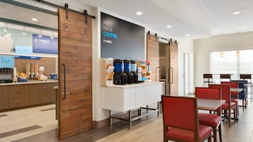 A modern cafe with a wooden accent wall, a coffee station, and red chairs.