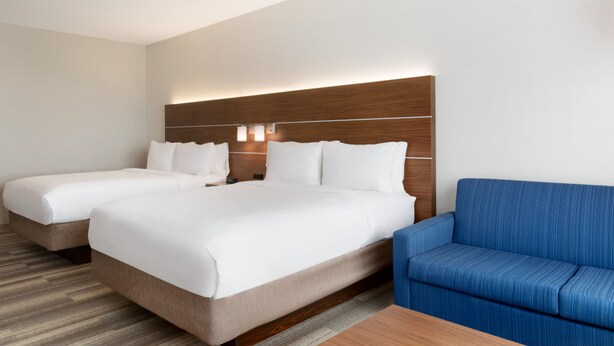 Une chambre d’hôtel avec deux lits, un canapé bleu et une tête de lit en bois.