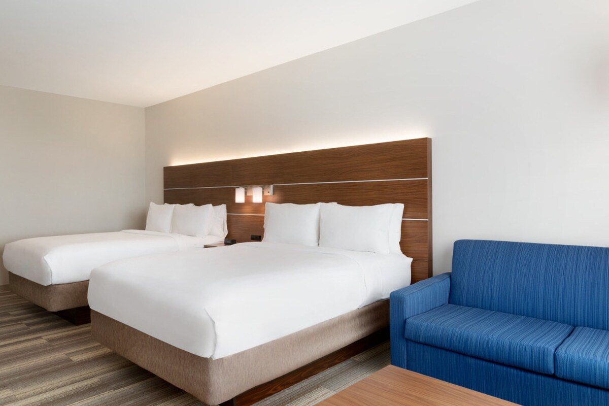 A hotel room with two beds, a blue sofa, and a wooden headboard.
