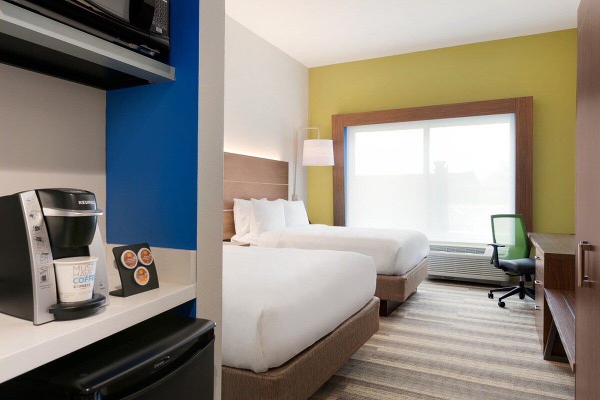 A hotel room with a bed, a desk with a coffee maker, a lamp, and a window.
