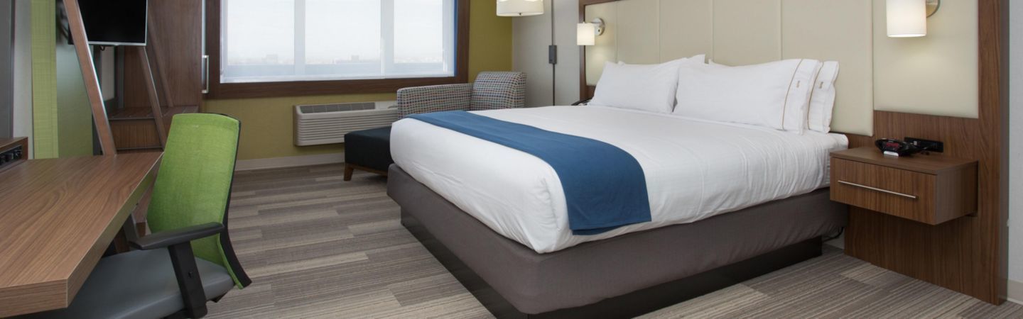 A hotel room with a bed, a desk, a chair, a TV, and a window.