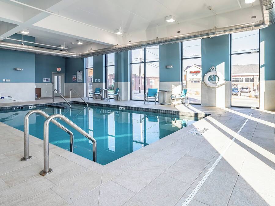 Una piscina interior con señalización de seguridad clara, una silla de salvavidas y vistas al exterior a través de amplias ventanas.