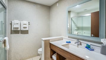 A modern bathroom with a large mirror, a sink with toiletries, and two towels hanging on the wall.