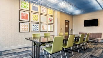 Uma sala de conferências com uma mesa comprida, cadeiras verdes, obras de arte emolduradas na parede e uma televisão de tela plana.