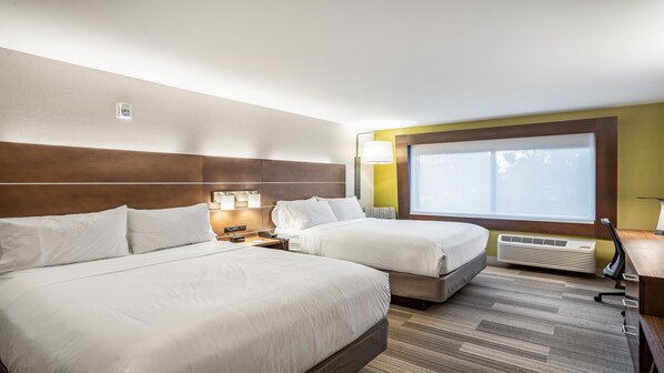 Quarto de hotel com duas camas, uma janela grande, aquecedor fixado na parede e mesa de cabeceira com luminária.
