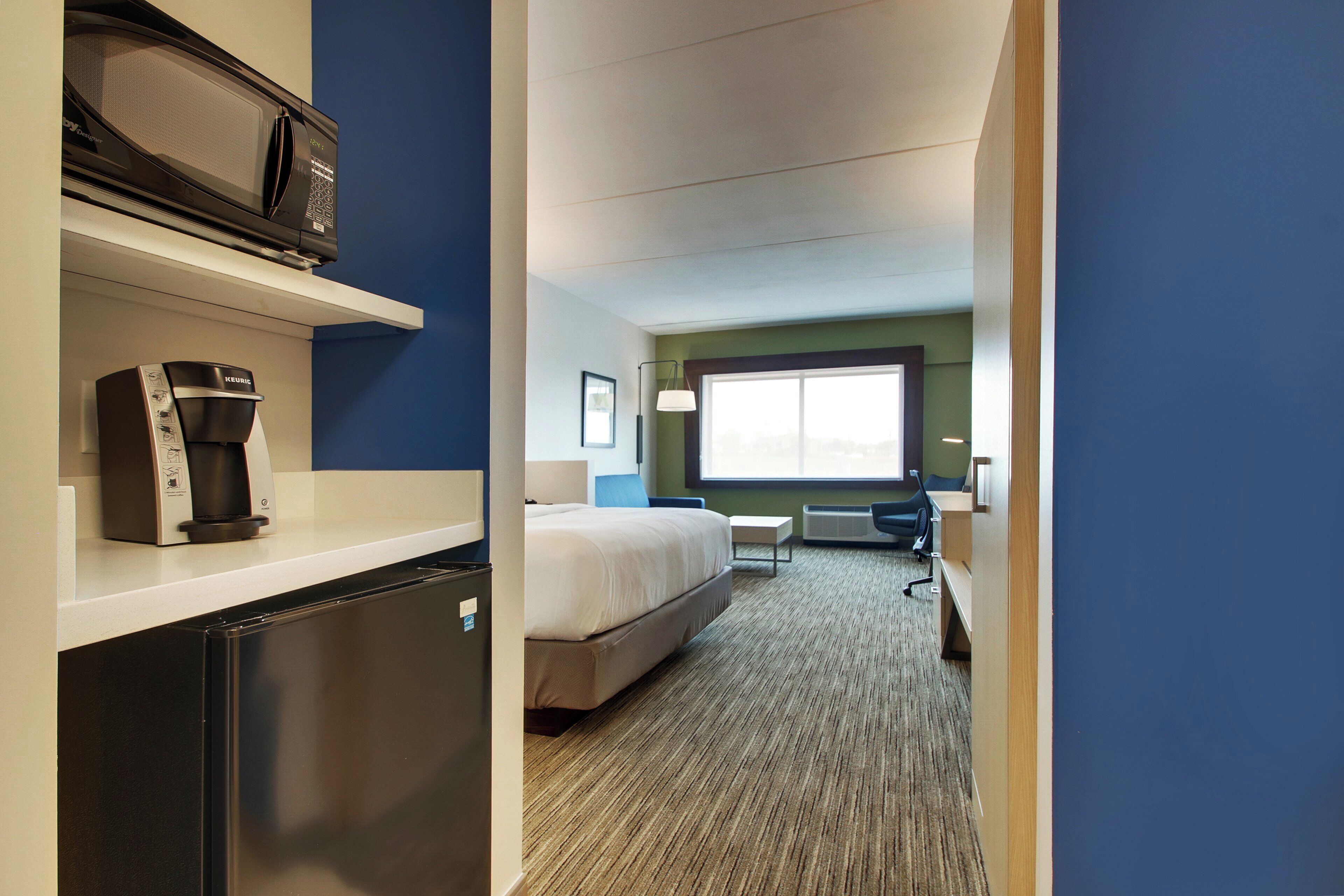 A hotel room with a bed, a desk, a microwave, and a refrigerator.