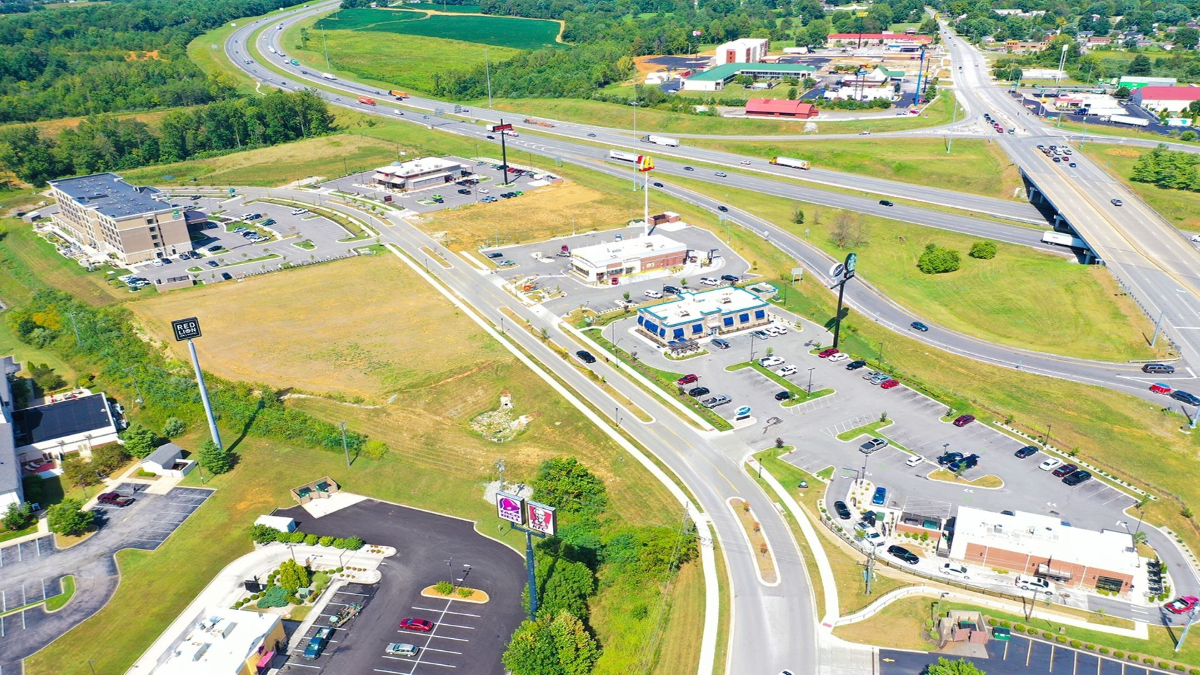 Vista aerea di un nodo autostradale con diverse corsie, strade di collegamento, aree di parcheggio e edifici commerciali.