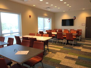 A conference room with multiple tables and chairs, large windows, a flat-screen TV, and a fire alarm on the wall. - Holiday Inn Express and Suites-Elizabethtown North by IHG (Elizabethtown)