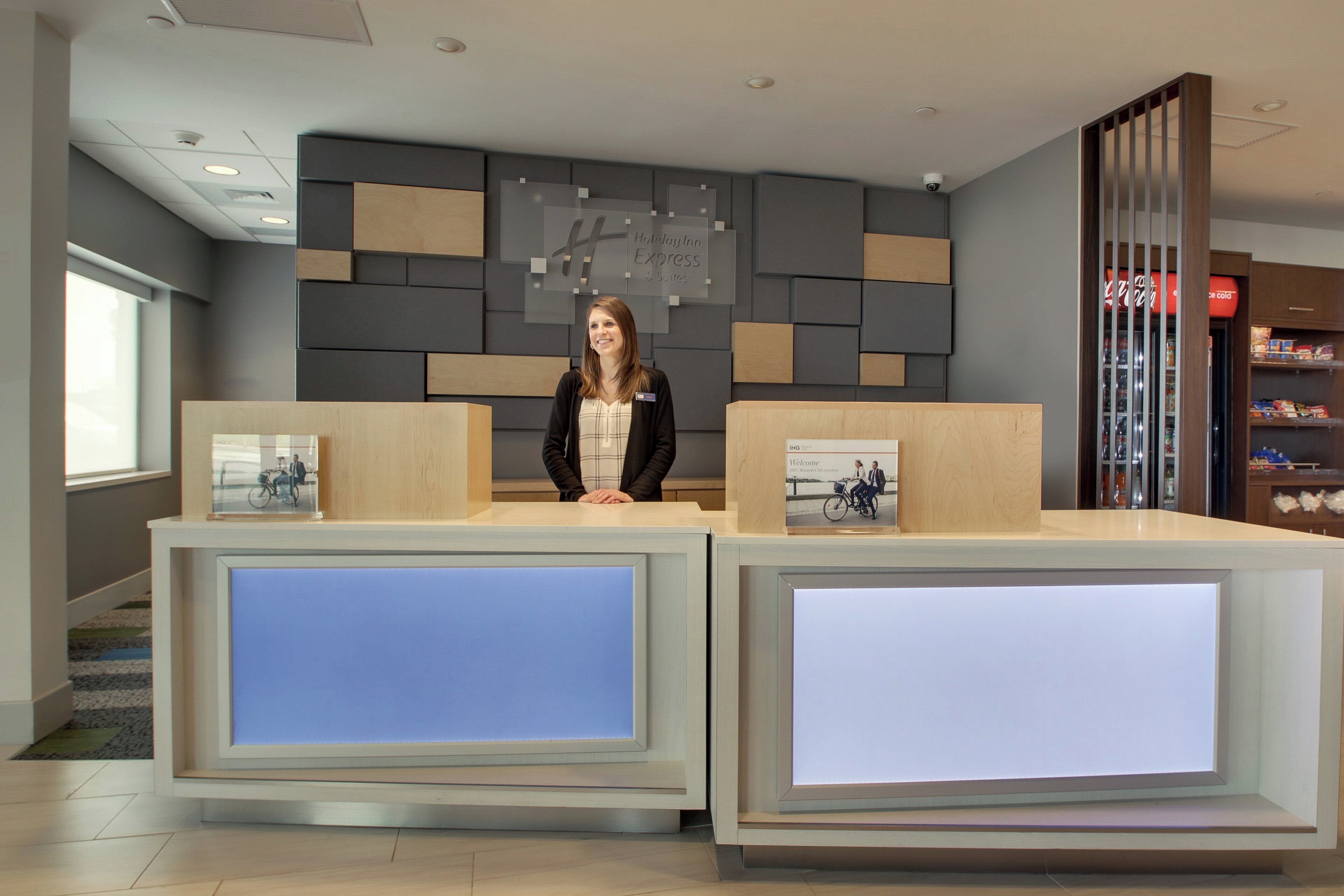Ein moderner Empfangstresen, über dem ein Schild mit der Aufschrift Holiday Inn Express & Suites zu sehen ist, und ein gekühlter Ausstellungsbereich zur Rechten.