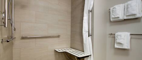 A shower area with a grab bar, a white towel rack, and a showerhead.