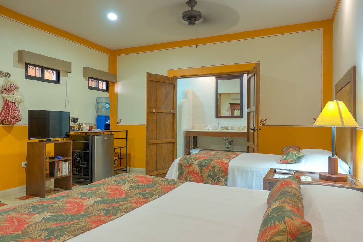 Habitació d'hotel amb dos llits, un escriptori, una televisió, un dispensador d'aigua i un mirall.