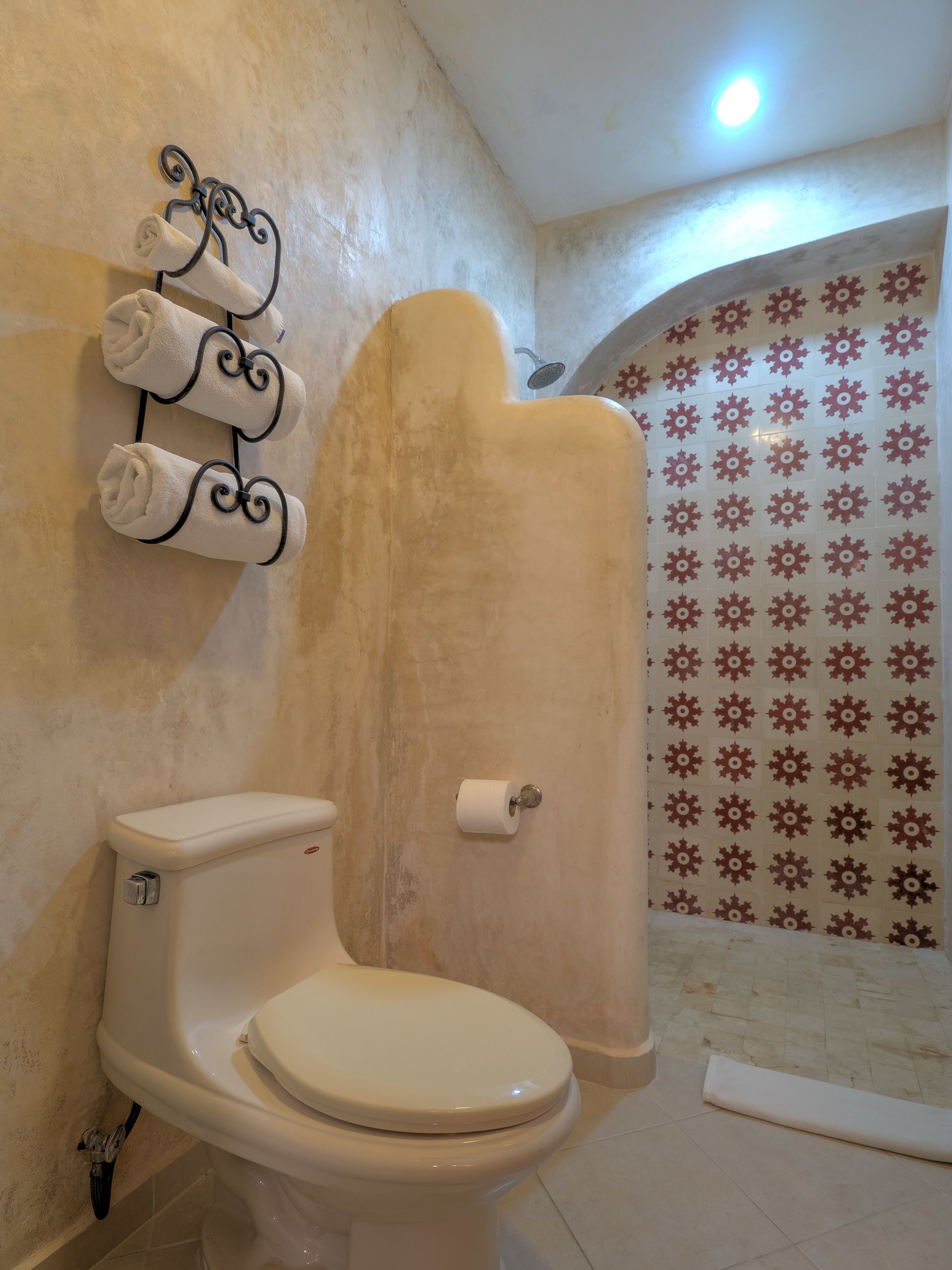 Un baño con inodoro, un perchero con toallas y una zona de ducha con azulejos estampados.