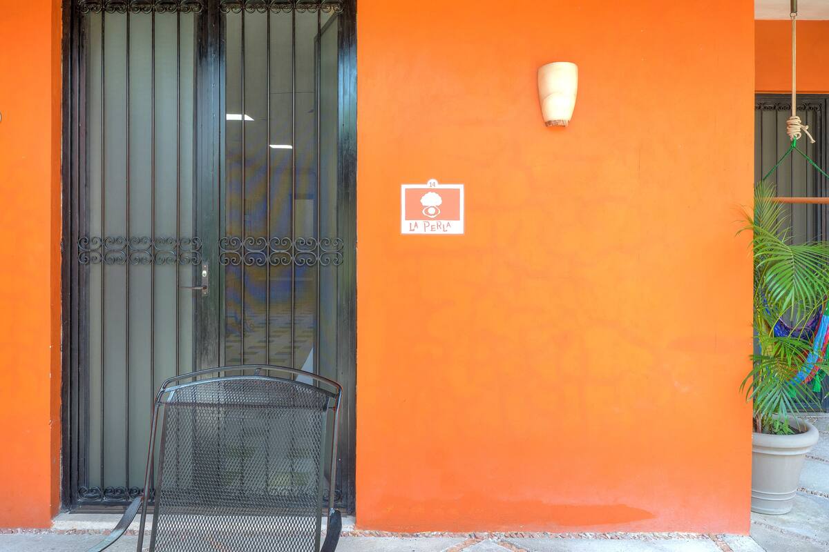Entrada d'un edifici amb una reixa de metall, una cadira i una planta en test.