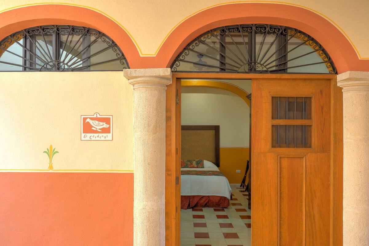 Una habitació d'hotel amb un terra de pissos de cuadros, un llit amb llençols i mantell blanc i vermell, i una porta de fusta.