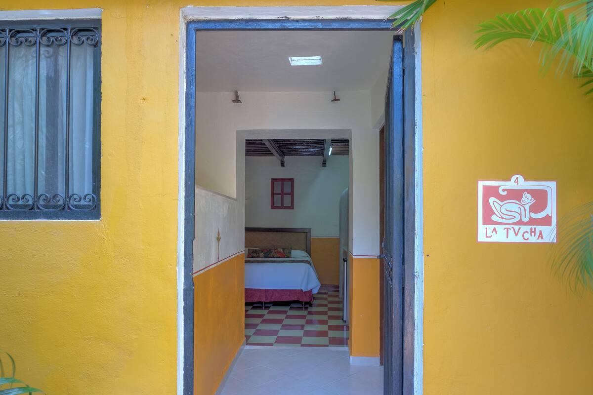 Un passadís estret que porta a una habitació amb un llit i un sòl d'escacs. Hi ha un cartell amb un personatge de dibuix animat i text visible a la paret.