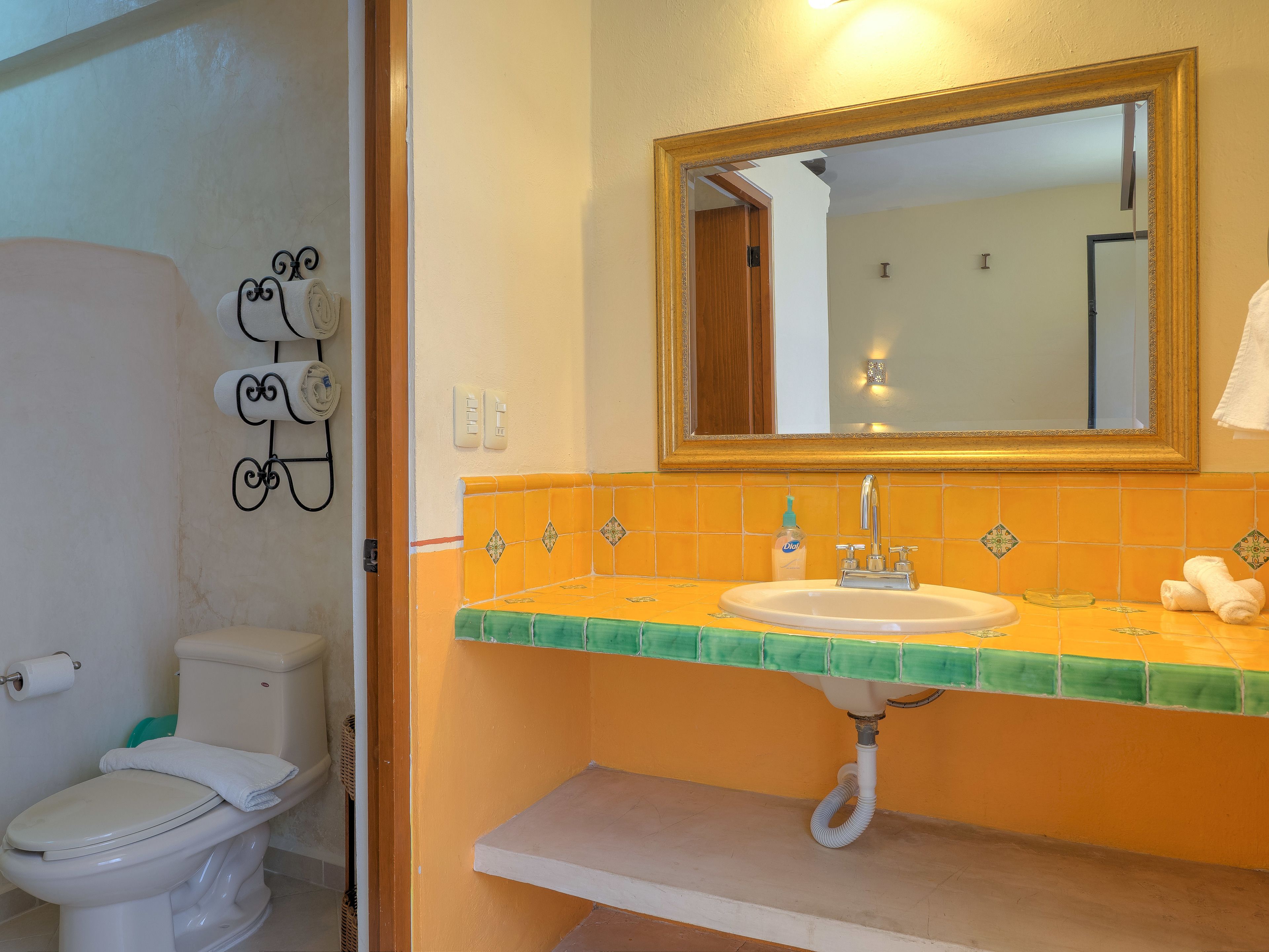 Une salle de bain avec des toilettes blanches, un lavabo doté d’un plan-vasque vert et un miroir au-dessus du lavabo.