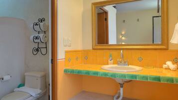 Un baño con inodoro blanco, lavabo con encimera verde y espejo sobre el lavabo.