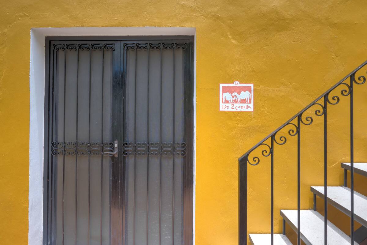 Paret groga amb una reixa de metall i una escala amb barana decorativa.