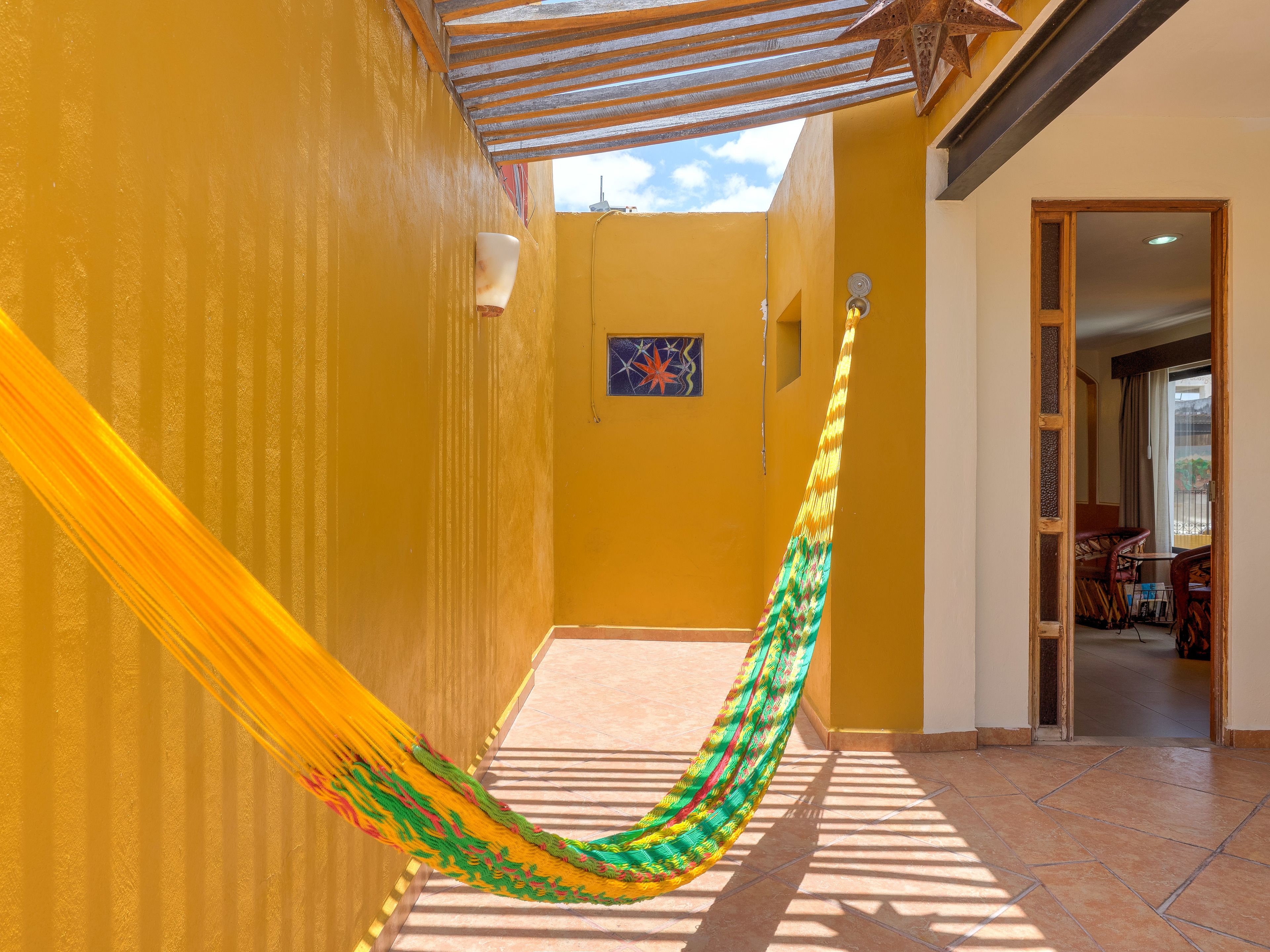 A hallway with yellow walls, a hammock, and a door leading to a room with a view.