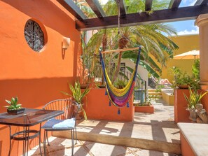 Une terrasse avec un hamac, une table et des chaises, ainsi que des plantes en pot.