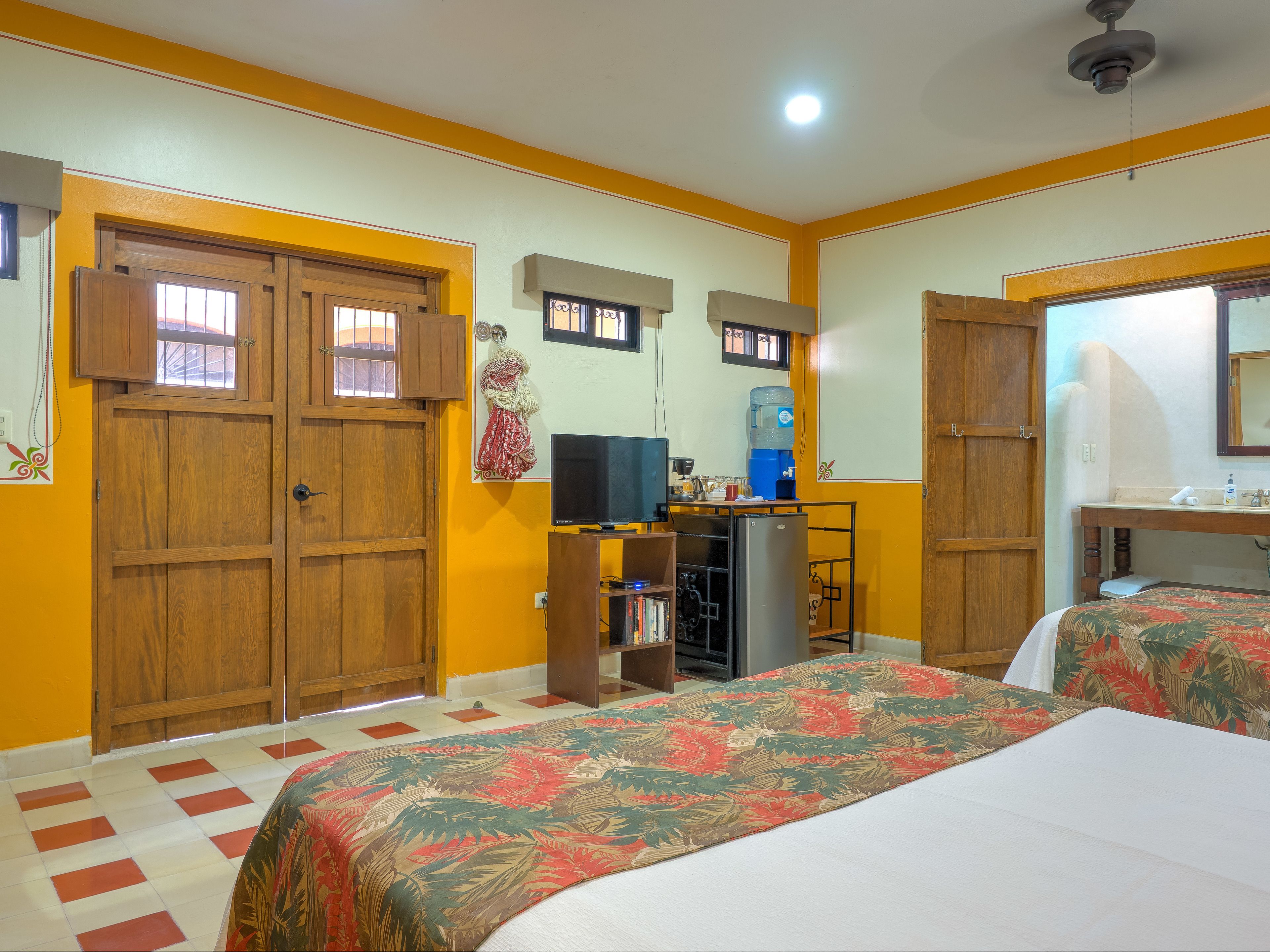 A room with two beds, a desk with a computer, a water dispenser, and a mirror.
